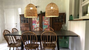 Comedor con una mesa grande, seis sillas de madera, dos lámparas colgantes de mimbre y un aparador con estampado floral.