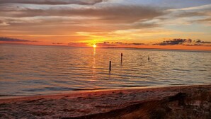 A sunset over a calm sea with a sandy beach in the foreground.