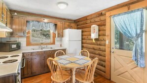 A compact kitchen with wooden cabinets, a white refrigerator, a stove, and a dining table with four chairs. - Carters Lake Lakeside Log Cabin #2 includes boat slip at the marina (Ellijay)