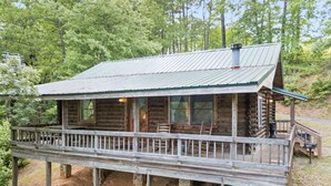 A log cabin with a wooden deck and a metal roof, surrounded by trees. - Carters Lake Lakeside Log Cabin #2 includes boat slip at the marina (Ellijay)