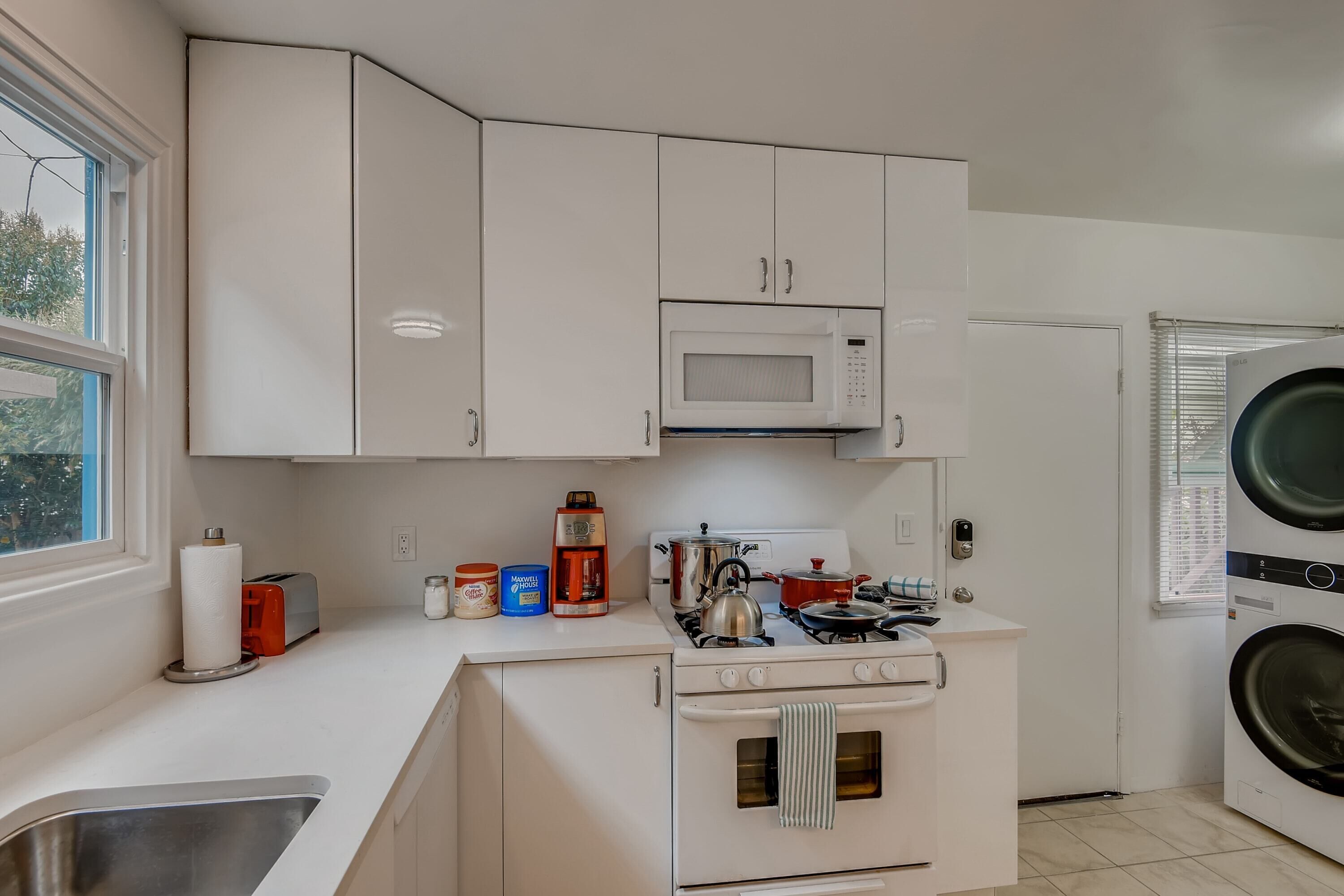 Una cocina compacta con armarios blancos, un microondas, una estufa y una lavadora.