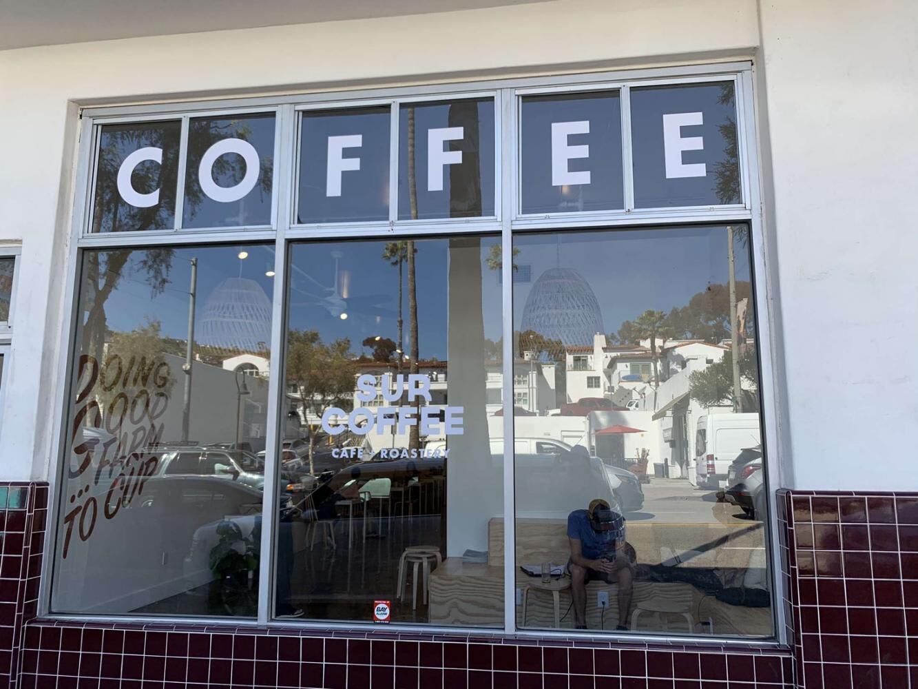 A coffee shop with a large window displaying the word "COFFEE" and a sign that reads "SUR COFFEE CAFE ROASTING".