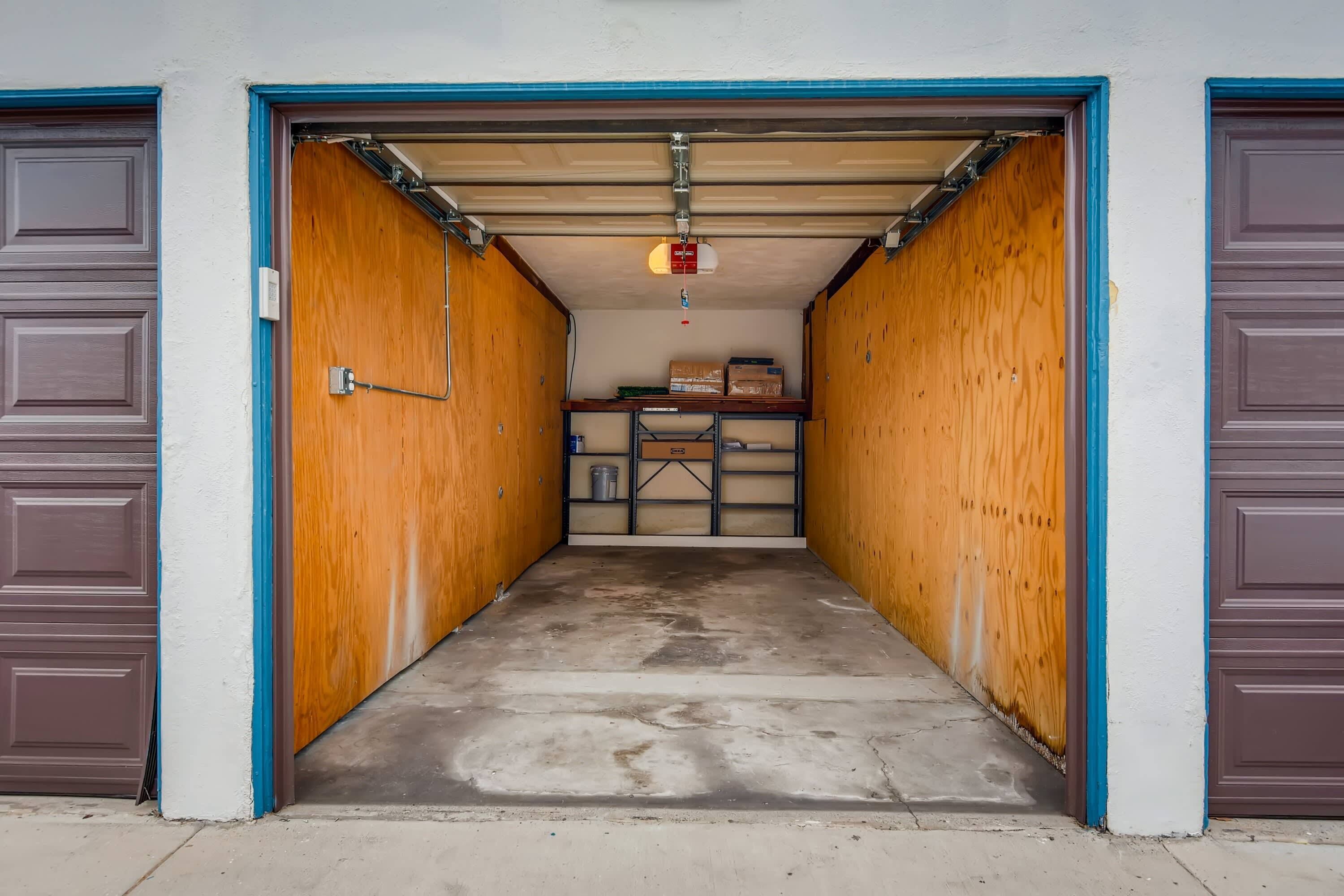 A garage with a concrete floor, wooden walls, and a metal shelf with boxes.