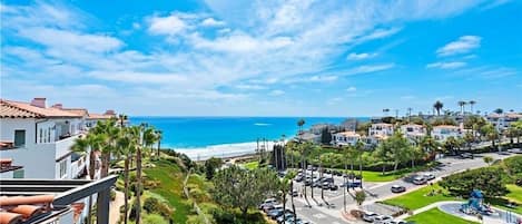A coastal residential area with a clear view of the ocean, a parking lot, and a mix of single and multi-story houses.