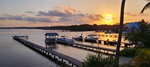 A marina with docks extending into calm waters, boats moored at the docks, and a sunset in the background.