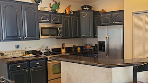 Una cocina con armarios oscuros, un refrigerador de acero inoxidable, un microondas y un lavamanos.