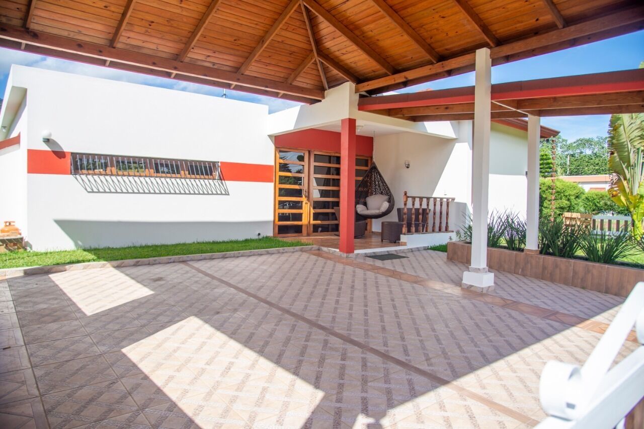 Ein überdachter Patio-Bereich mit gefliestem Boden, Holzboden und einem weißen Gebäude mit roten Akzenten.