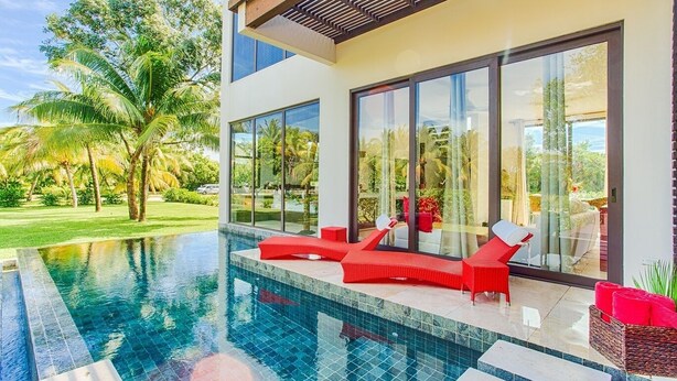 Una casa moderna con piscina, sillones reclinables rojos y grandes puertas de cristal.