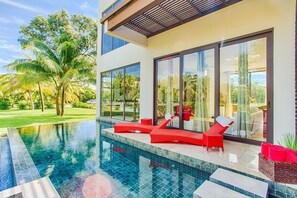 Ett modernt hus med en swimmingpool, röda solstolar och stora glasdörrar.