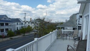 A porch with a white railing, a few chairs, and a view of a street with houses.