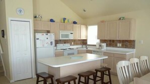A kitchen with a central island, bar stools, and a dining area with chairs.