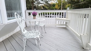 A white wooden deck with two ornate metal chairs and a small round table, surrounded by a white picket fence.