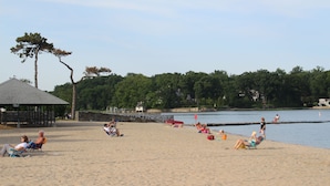 A beach with people relaxing on the sand, a pier, and a lake in the background.