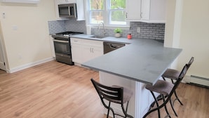 A modern kitchen with white cabinets, a stainless steel stove, a microwave, and a large island with bar stools.