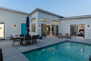 Una casa moderna con piscina, zona de estar al aire libre y un gran ventanal que da a una sala de estar.