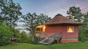 A small, single-story cabin with a porch and a staircase leading to a deck, surrounded by trees and a body of water. - Carters Lake, Lakeside Cabin #9, includes free boat slip at the Marina (Ellijay)
