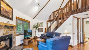 A living room with a stone fireplace, a television, a blue sofa, and a wooden staircase. - Carters Lake, Lakeside Cabin #9, includes free boat slip at the Marina (Ellijay)