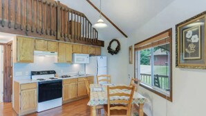 A kitchen with wooden cabinets, a stove, and a microwave. There is a dining table with chairs and a window with a view of the outside. - Carters Lake, Lakeside Cabin #9, includes free boat slip at the Marina (Ellijay)