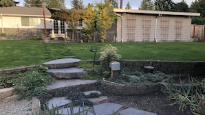 Un patio trasero con un camino de piedra, un pequeño jardín y una valla de madera.