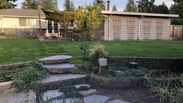 Un patio trasero con un camino de piedra, un pequeño jardín y una valla de madera.