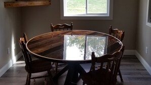 A dining room with a round glass table surrounded by wooden chairs, a ceiling fan, and a window with a view of a yard.
