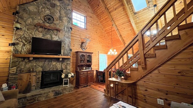 A spacious interior with a stone fireplace, wooden walls, a mounted television, and a staircase.