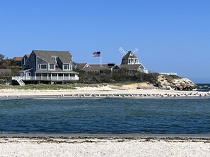 A coastal house with a windmill, a beach in the foreground, and a clear sky. - New updates! Relaxing cottage, Walk to Beach 10 min. to South Village Beach 🏖️  (West Dennis)