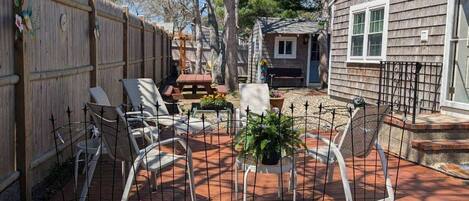 A backyard with a wooden fence, a patio with white chairs and a table, and a small shed.
