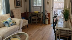 Una sala de estar acogedora con un sofá, una mesa de centro de vidrio, una mesa de comedor con sillas, un escritorio pequeño y una ventana con cortinas.