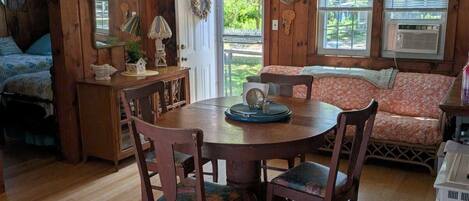 A cozy cabin interior with a wooden dining table, chairs, a bench, and a small kitchen area.