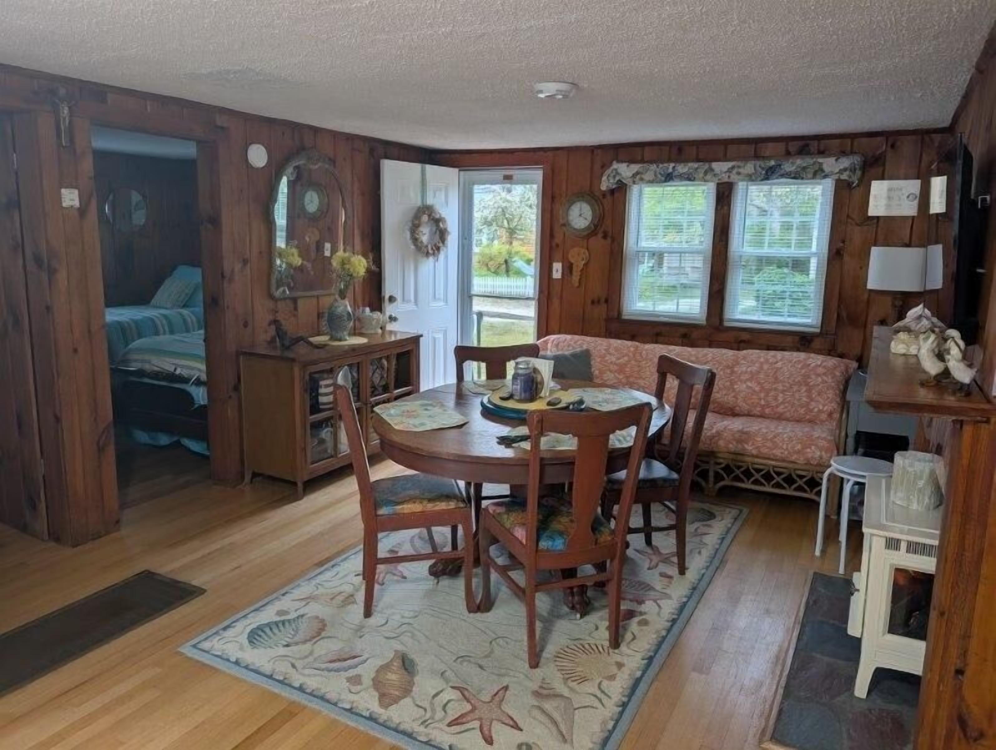 Interior acogedor de una cabaña con una mesa de madera, sillas, un sofá y una pequeña cocina.