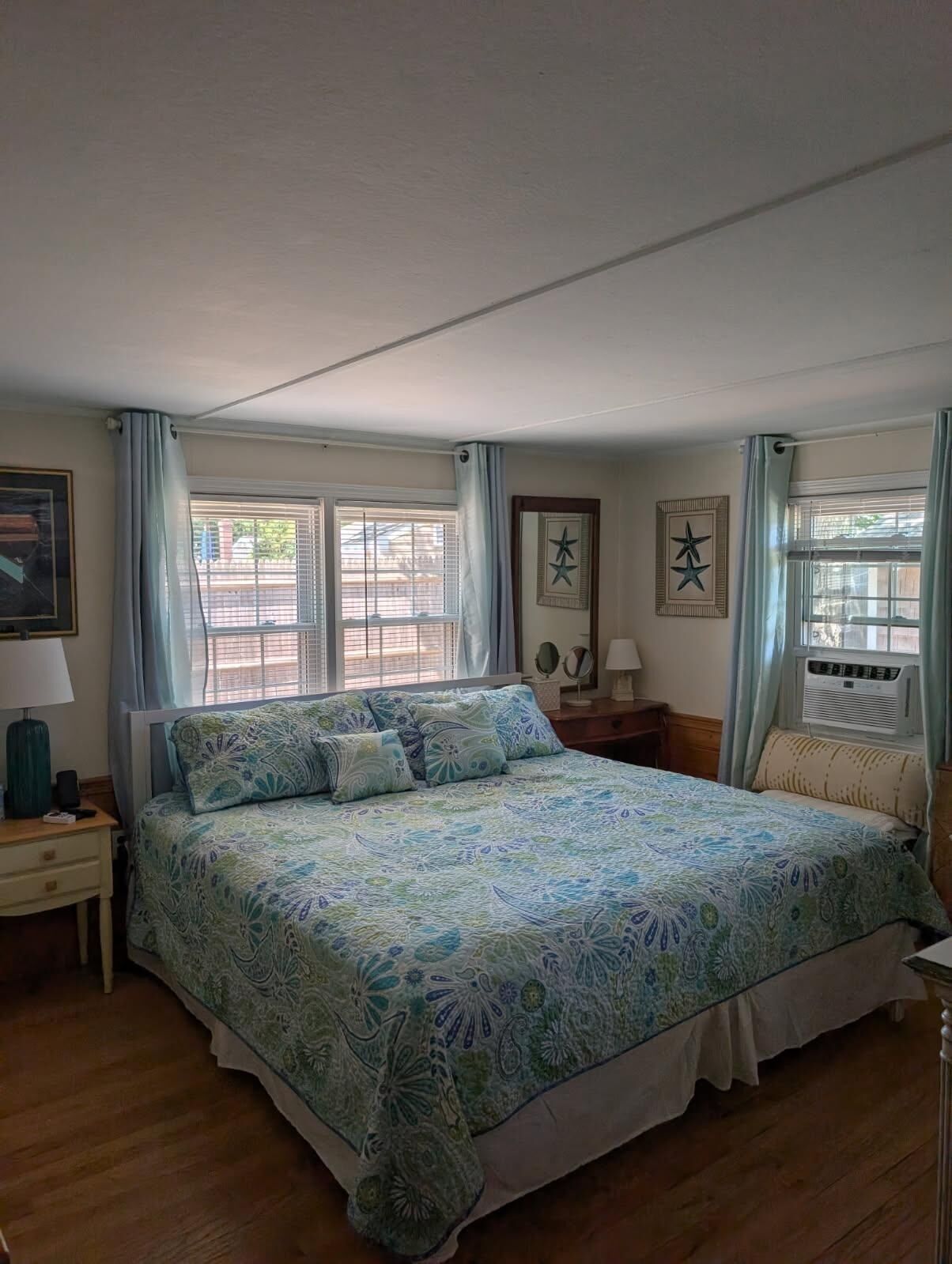 Un dormitorio con una cama grande, dos mesitas de noche y un ventanal con cortinas.