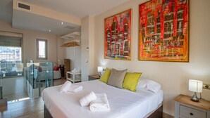 A hotel room with a large bed, a bedside table, a chair, a desk, and two abstract paintings on the wall. - Loft Space - Time in Cádiz (Cádiz)