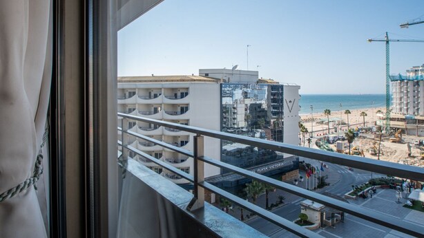 A balcony with a view of a beach, buildings, and a construction site. - Loft Space - Time in Cádiz (Cádiz)