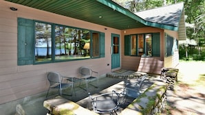 A covered outdoor seating area with chairs and a stone wall, overlooking a body of water. - Kitty Foye House on Upper Eau Claire Lake in Barnes (Barnes)