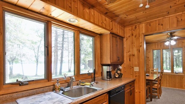 A wooden cabin kitchen with a sink, stove, and dining area. - Kitty Foye House on Upper Eau Claire Lake in Barnes (Barnes)