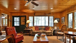 A cozy cabin interior with wooden walls and ceilings, a leather armchair, a sofa, a dining table, and a ceiling fan. - Kitty Foye House on Upper Eau Claire Lake in Barnes (Barnes)