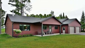 A two-story house with a red exterior, a garage, and a patio with outdoor furniture. - Sugar Bay Sweets - Lake Namakagon (Cable)