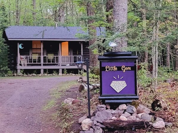 A cabin with a porch and a sign reading "Little Gem."