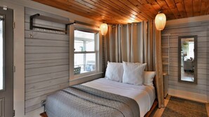 Un dormitorio con cama, techo de madera, ventana con cortinas y un espejo en la pared.