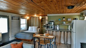 Habitación compacta con cama, una mesa de comedor con sillas, kitchenette con refrigerador y microondas, y ventana con cortinas.
