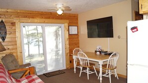 Un interior de cabaña acogedor con detalles de madera, una mesa de comedor con sillas, un ventilador de techo y un refrigerador.