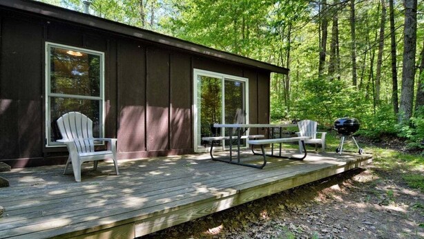 Una cabaña con terraza, dos sillas tipo Adirondack, una mesa de picnic y una parrilla.