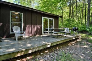 A cabin with a deck, two Adirondack chairs, a picnic table, and a grill.