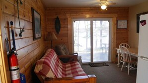 Un acogedor interior de cabaña con detalles de madera, un sofá a cuadros, una mesa de comedor con sillas y un ventanal corredizo que da a un espacio exterior.