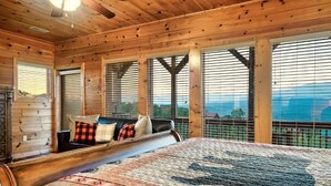 Un dormitorio de cabaña de troncos con una cama grande, un aparador de madera y vistas a las montañas a través de las ventanas.