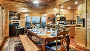 Interior de una cabaña de madera con comedor, cocina y chimenea.
