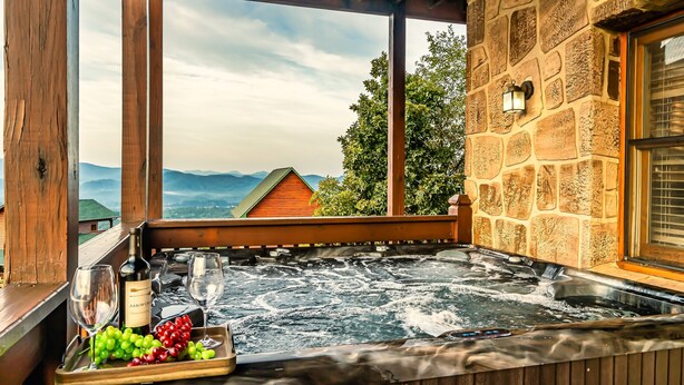 Un jacuzzi con cubierta de madera, una botella de vino Arrow Creek y una bandeja de uvas.