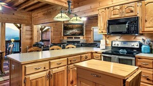 Una cocina de estilo cabaña de madera con una isla grande, armarios de madera, un microondas negro, una estufa y un colgador de luces.