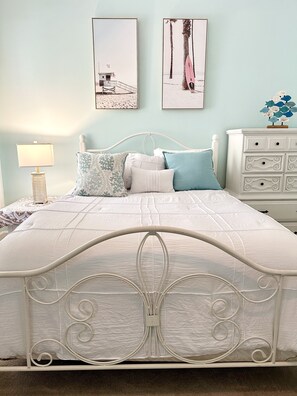 A neatly made bed with a white metal frame and a quilted white mattress.